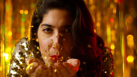 Woman-Celebrating-At-Party-Or-Club-Blowing-Handful-Of-Gold-Glitter-Towards-Camera